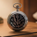 Silver pocket watch with a black and white floral design on a white background
